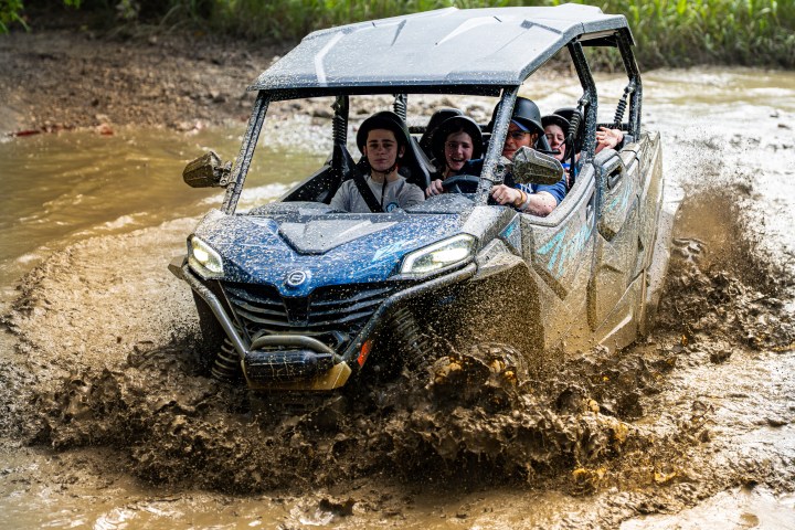 Four people riding an ATV through muddy water.