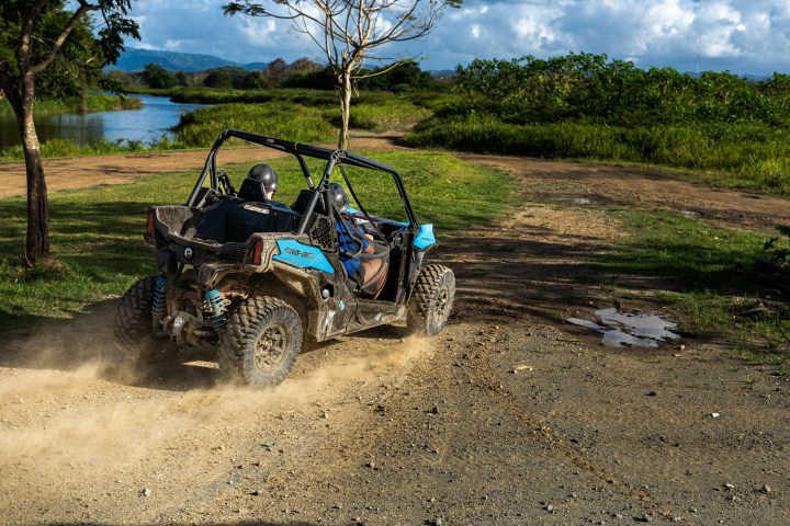 ATV driving on a dirt path near a river with lush greenery.