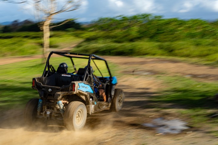 Two people driving a dune buggy on a dirt path with motion blur.