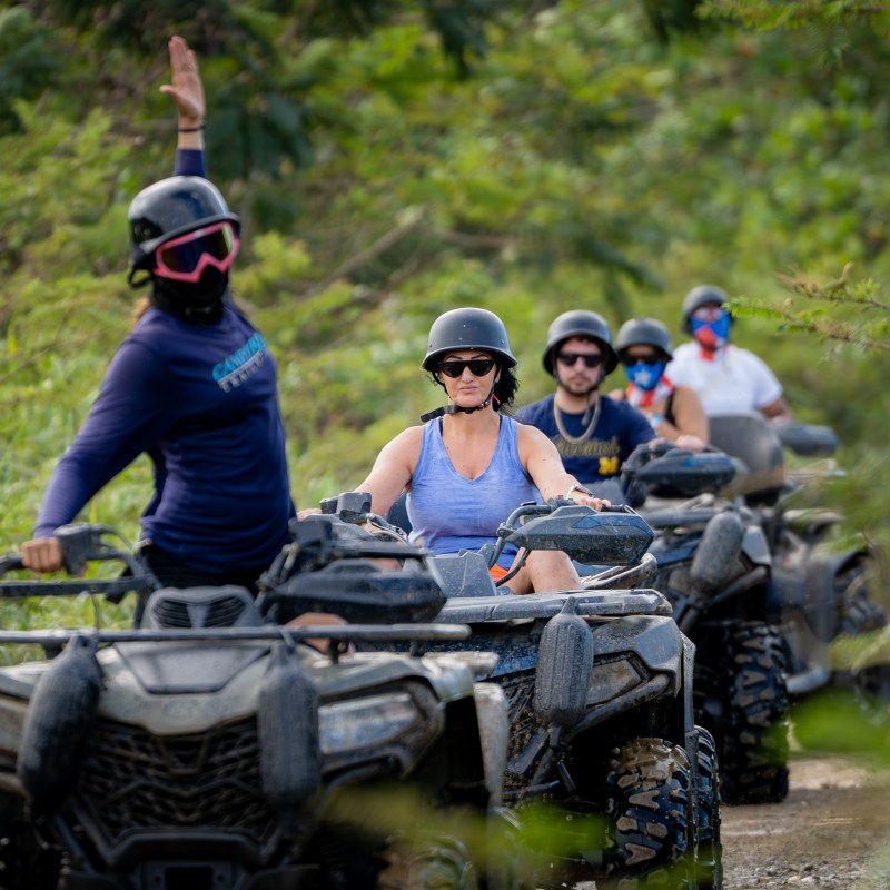 Group of people riding ATVs on a dirt path wearing helmets.